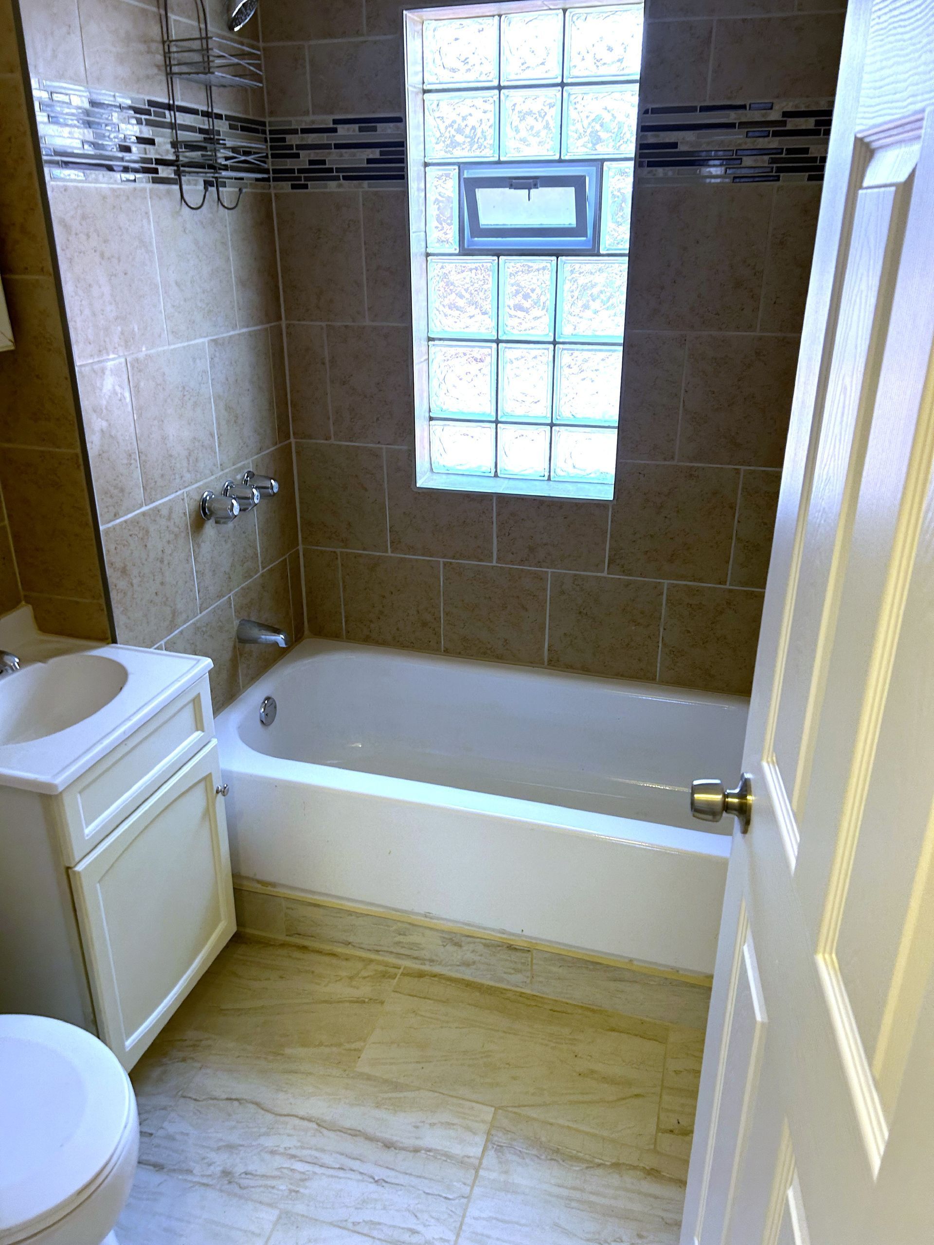 Bathroom with white tub, vanity, and toilet; beige tile walls and floor.