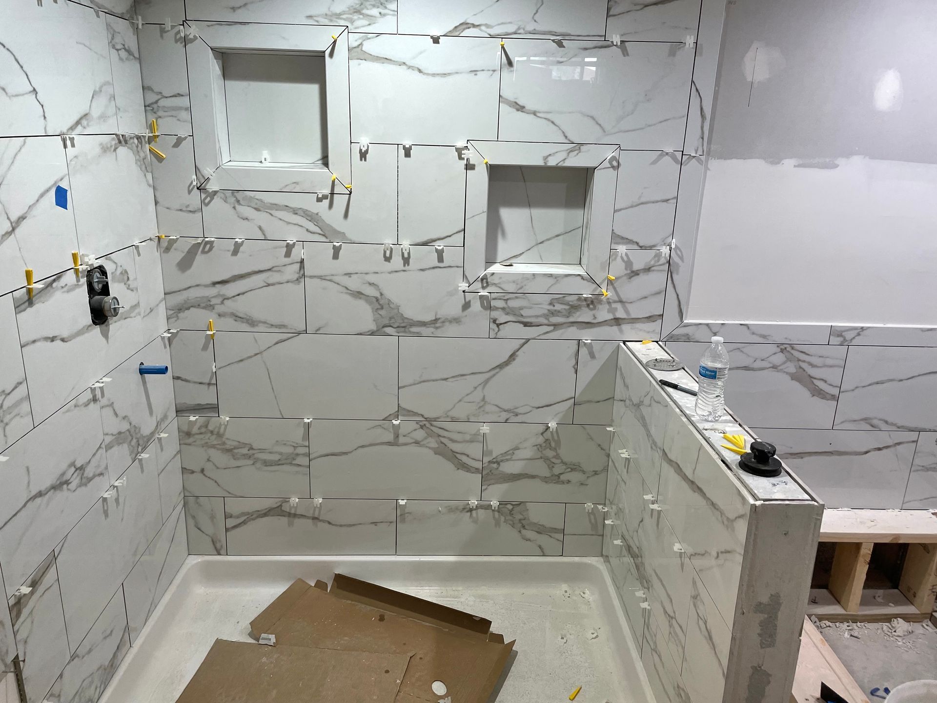 Bathroom renovation in progress, featuring white marble-look tiles, shower niche, and shower pan.