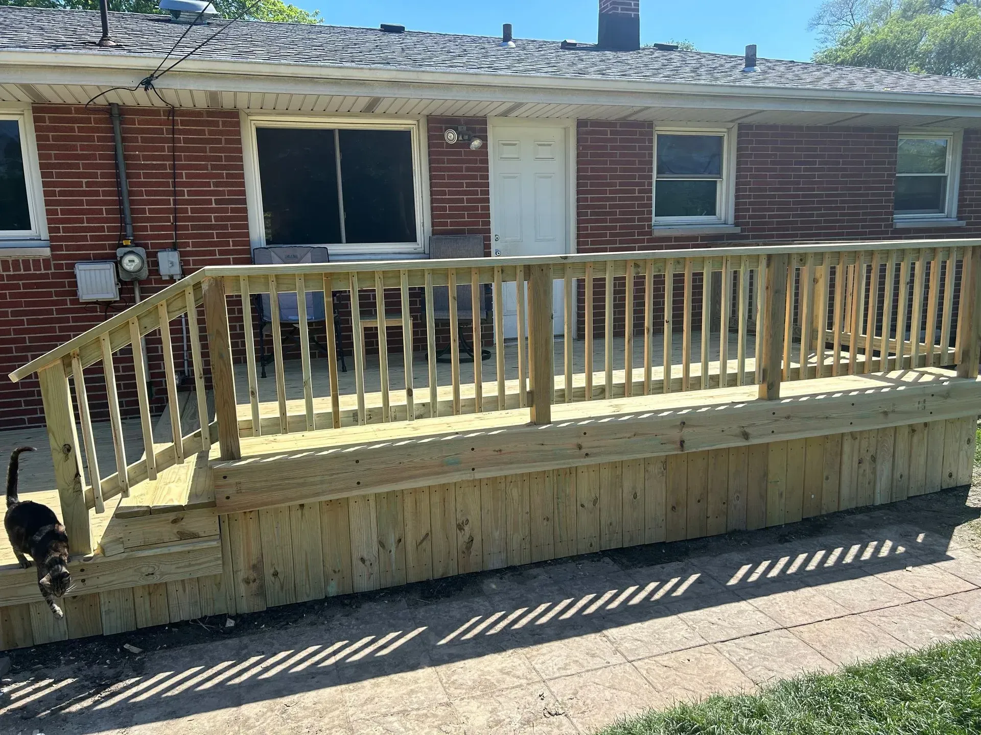 Newly built wooden deck attached to a brick house, with a cat walking on a paved pathway.