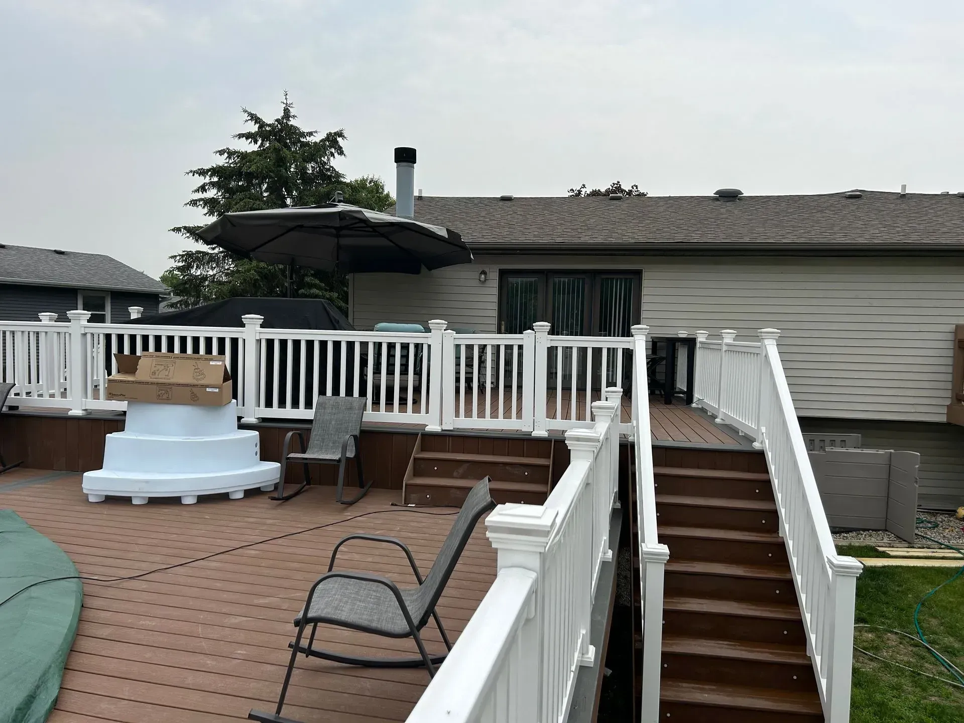 Brown deck with white railing and steps leading to a backyard, with an umbrella and house.