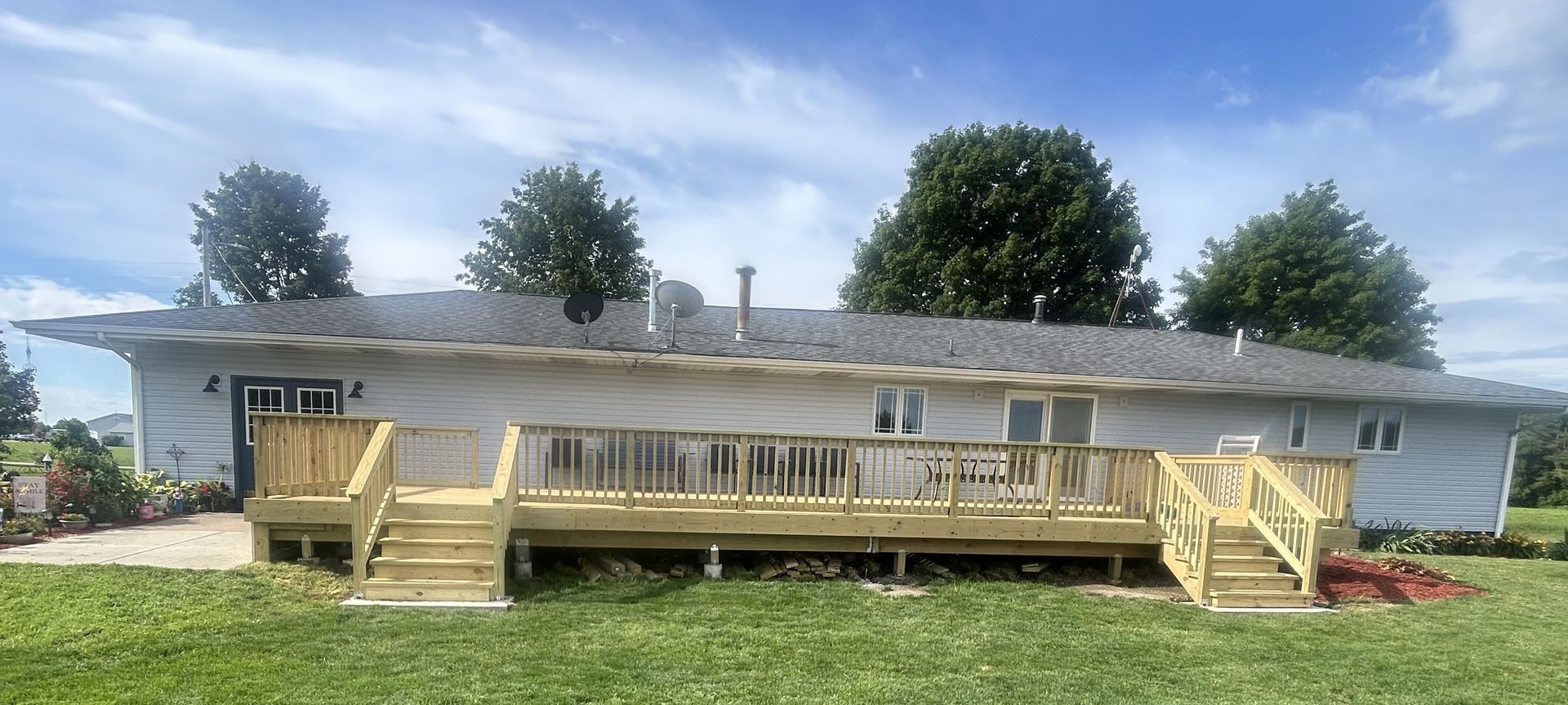 Single-story white house with a wide wooden deck and steps in a grassy yard under a partly cloudy sky