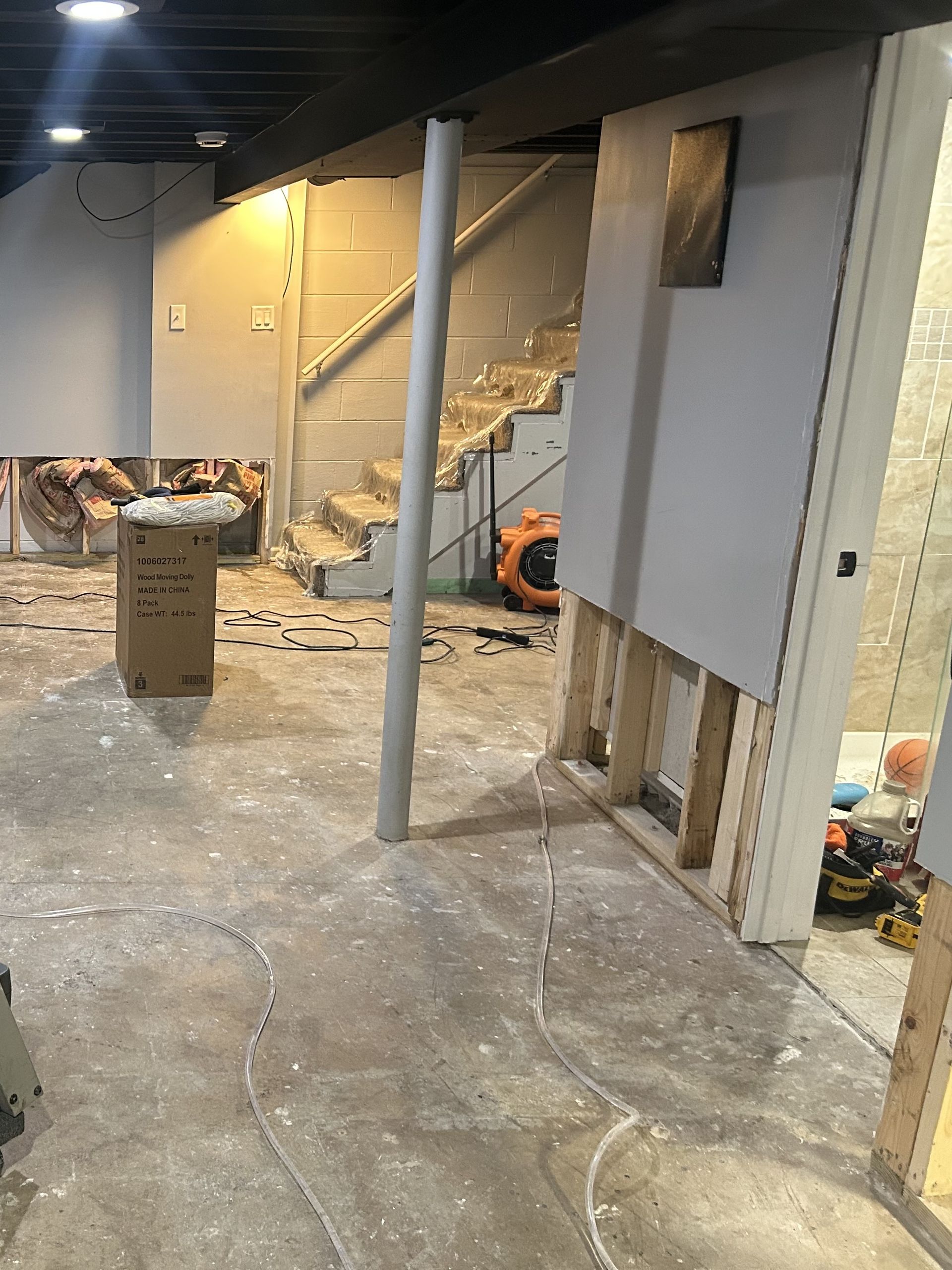 Basement under renovation with exposed studs, drywall, support beam, and stairs.