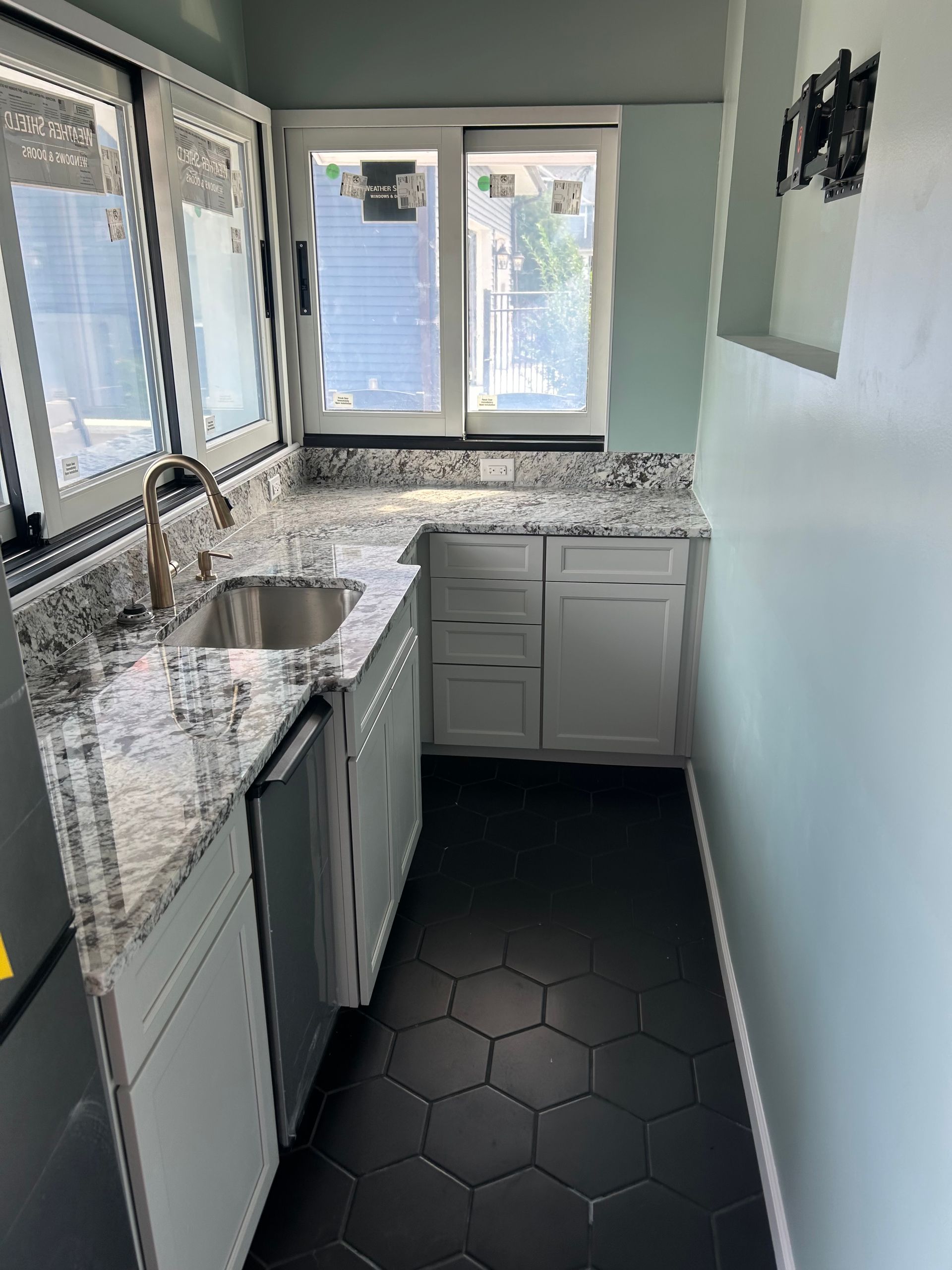 Small kitchen with white cabinets, granite countertop, black hexagon tile floor, and light blue walls.