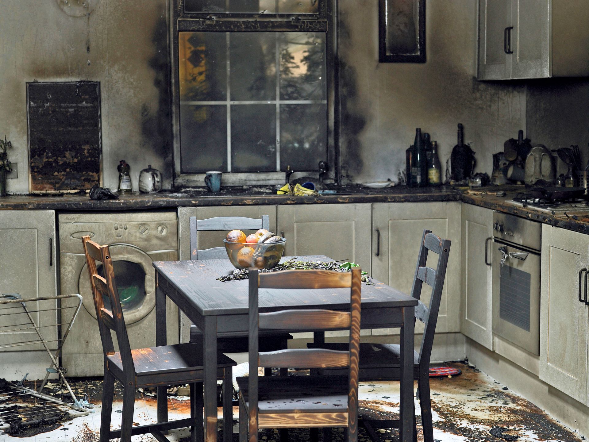 Kitchen destroyed by fire; furniture, appliances, and walls are charred black.