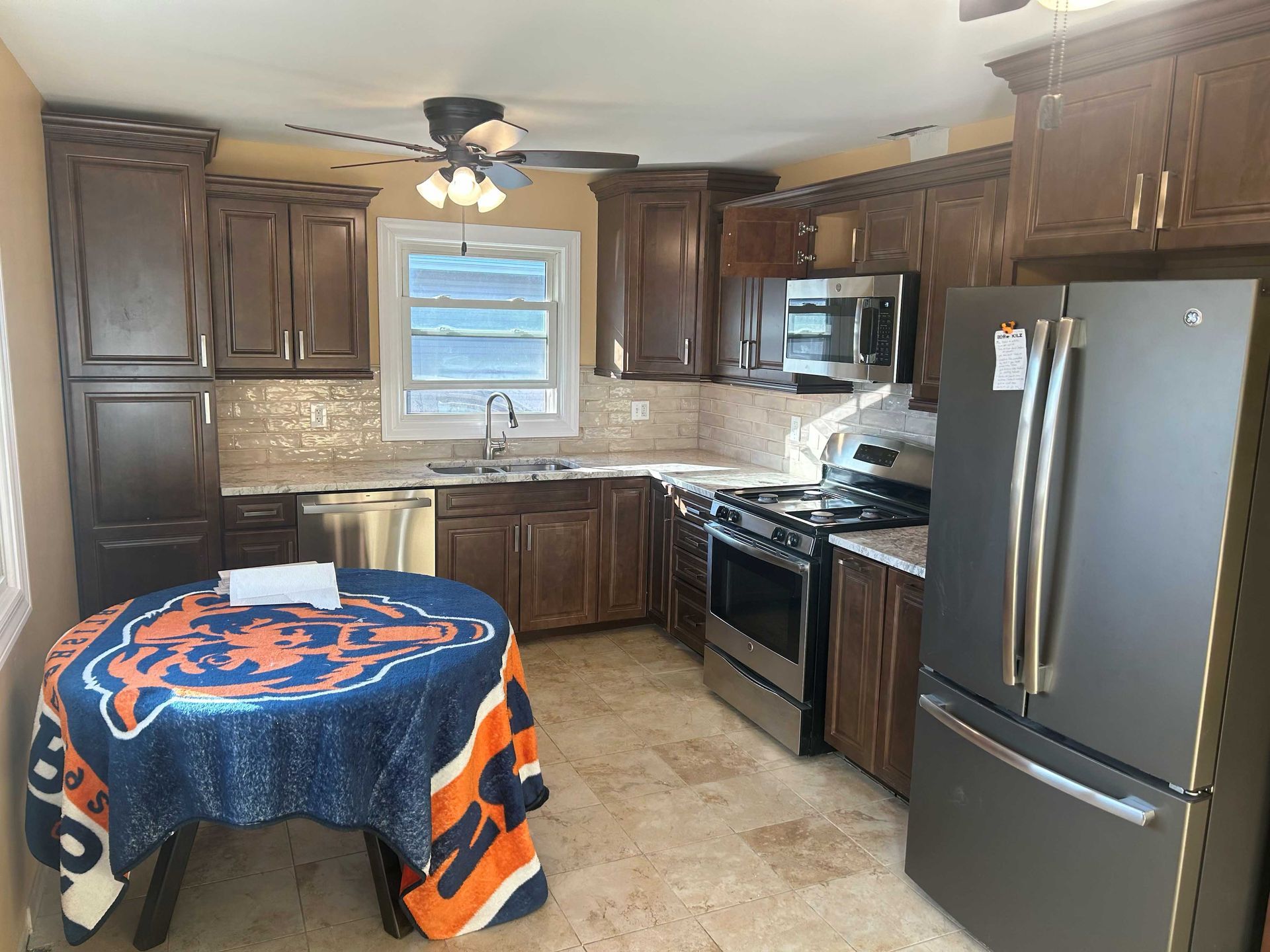Kitchen with brown cabinets, stainless steel appliances, and a table with a blue and orange tablecloth.