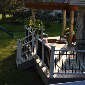 Deck with white railings, black balusters, and a pergola; green lawn and trees in the background.