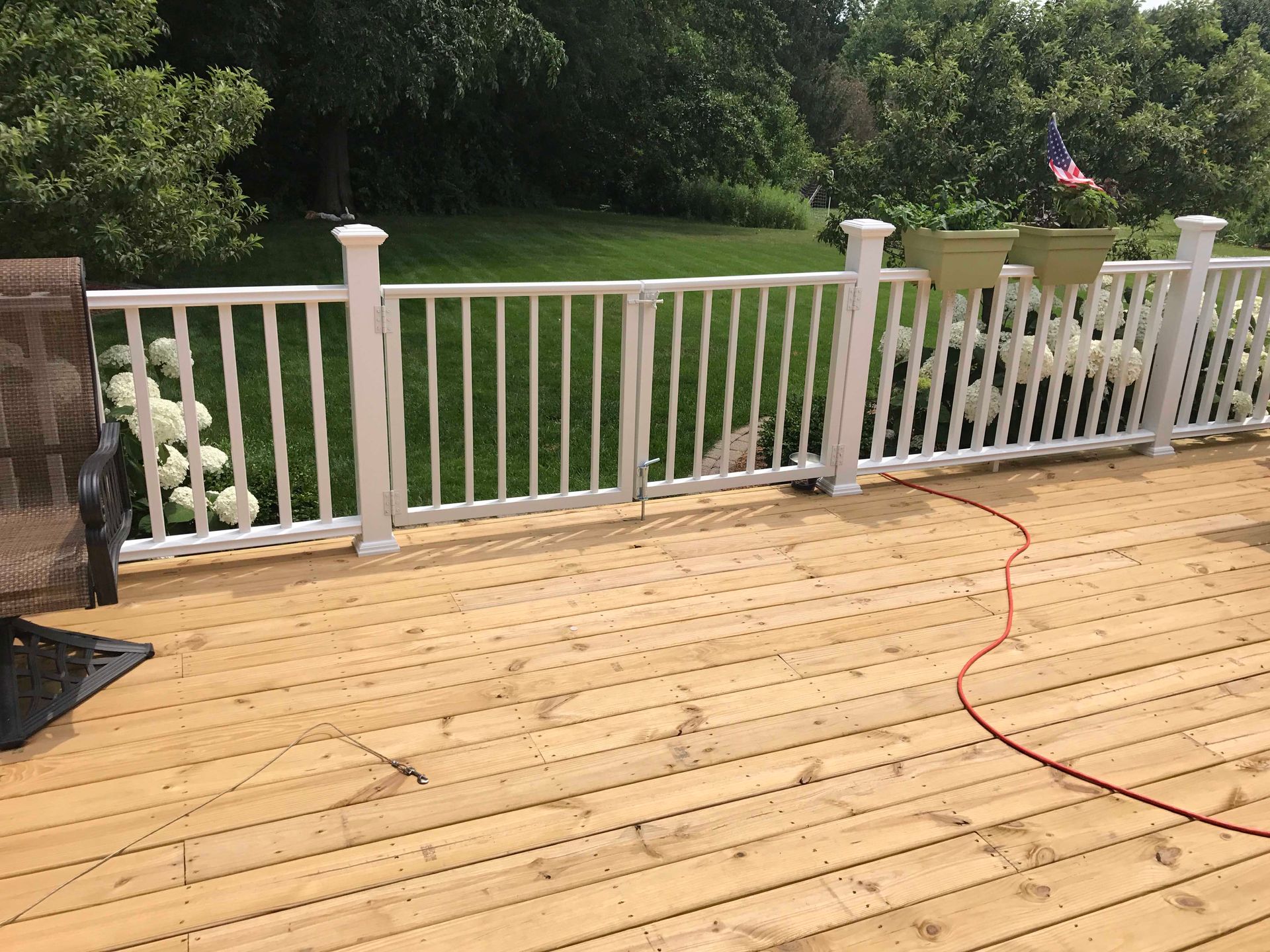 Wooden deck with white railing, green plants, and a red hose in a yard.