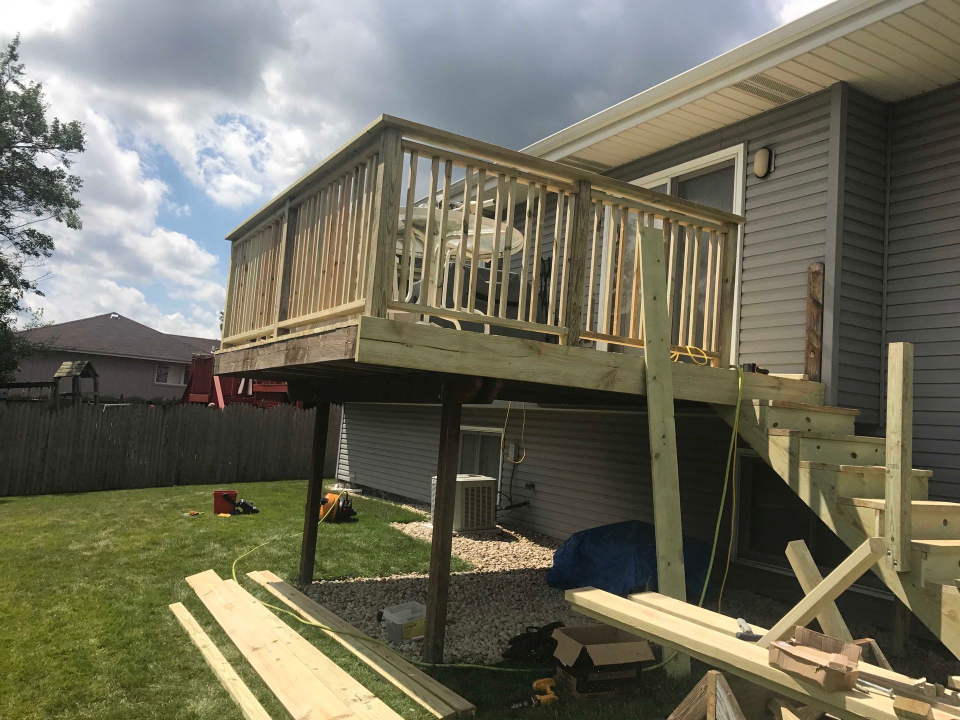 Wooden deck under construction with stairs, railing, and support posts in a backyard.