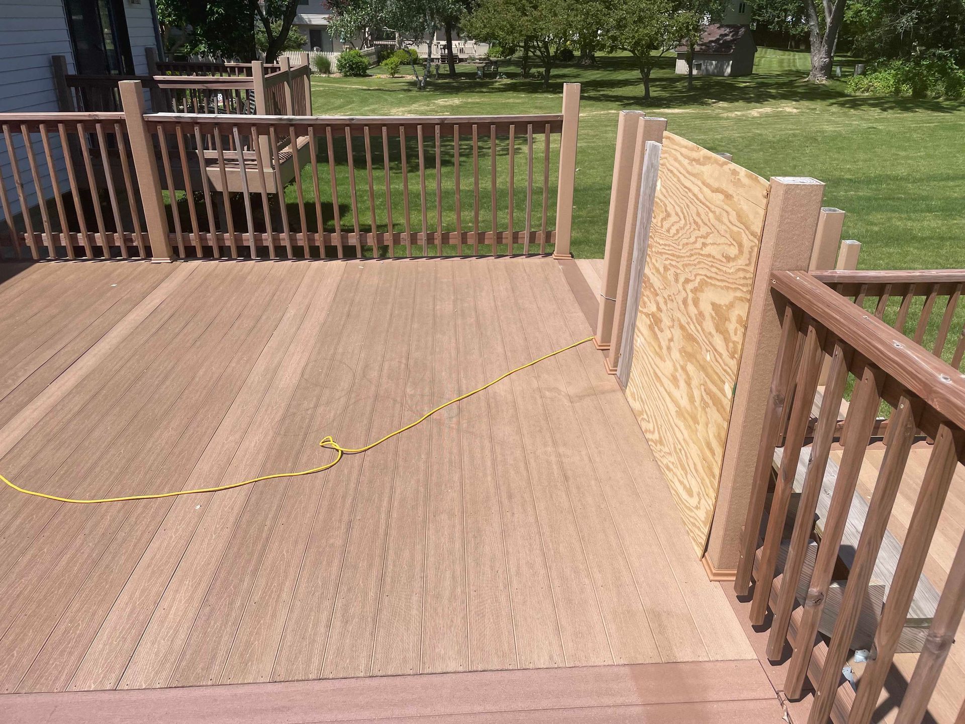 Wooden deck with railings, plywood leaning against post, yellow extension cord.