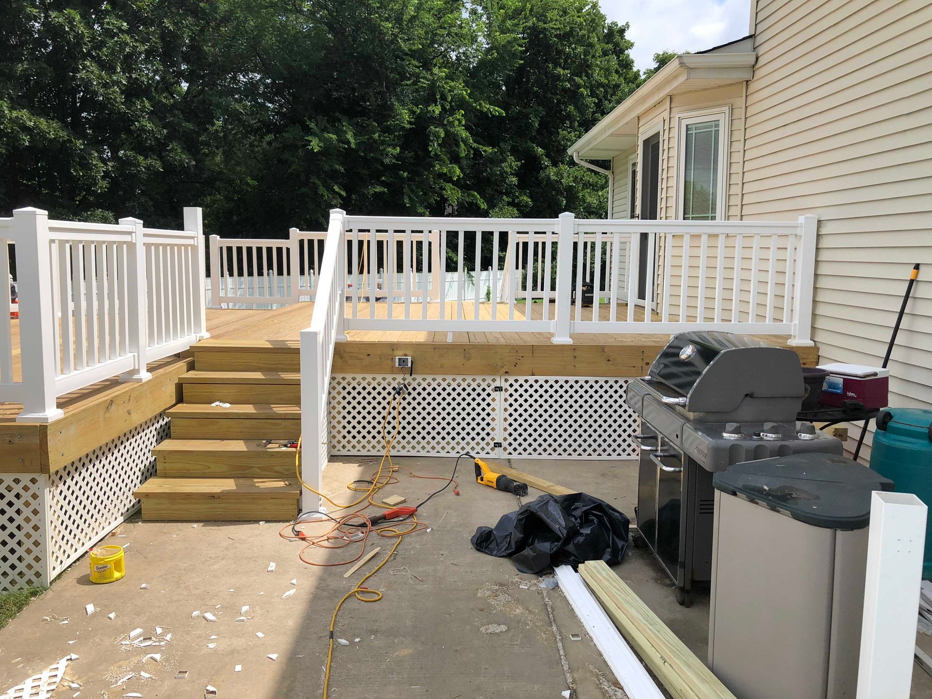 Wooden deck with white railing, stairs, and a grill. Construction tools and debris are visible.