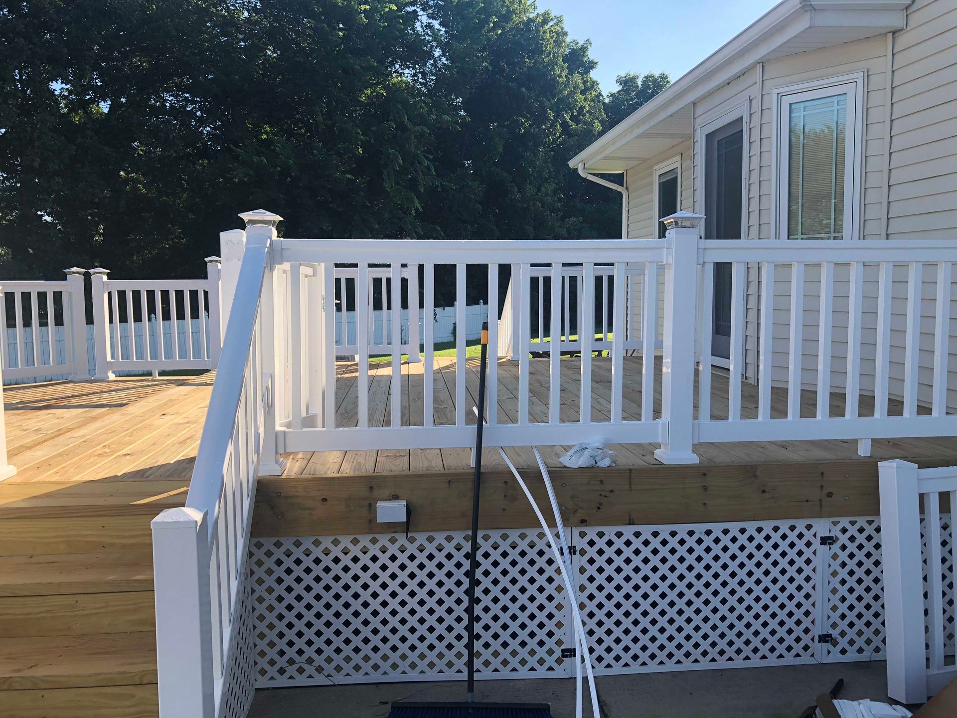 White deck with railing, partially surrounded by trees, next to a house.