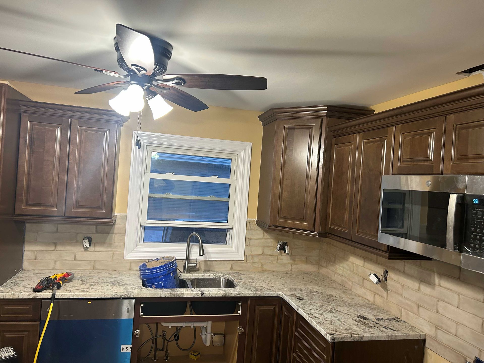Kitchen under renovation with new cabinets, countertops, backsplash, sink, and microwave.