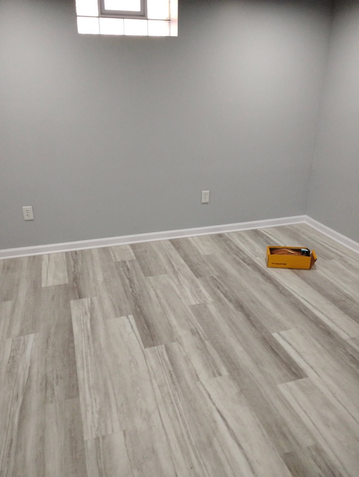 A room with gray walls and wood-look flooring; a small box sits on the floor near the corner.
