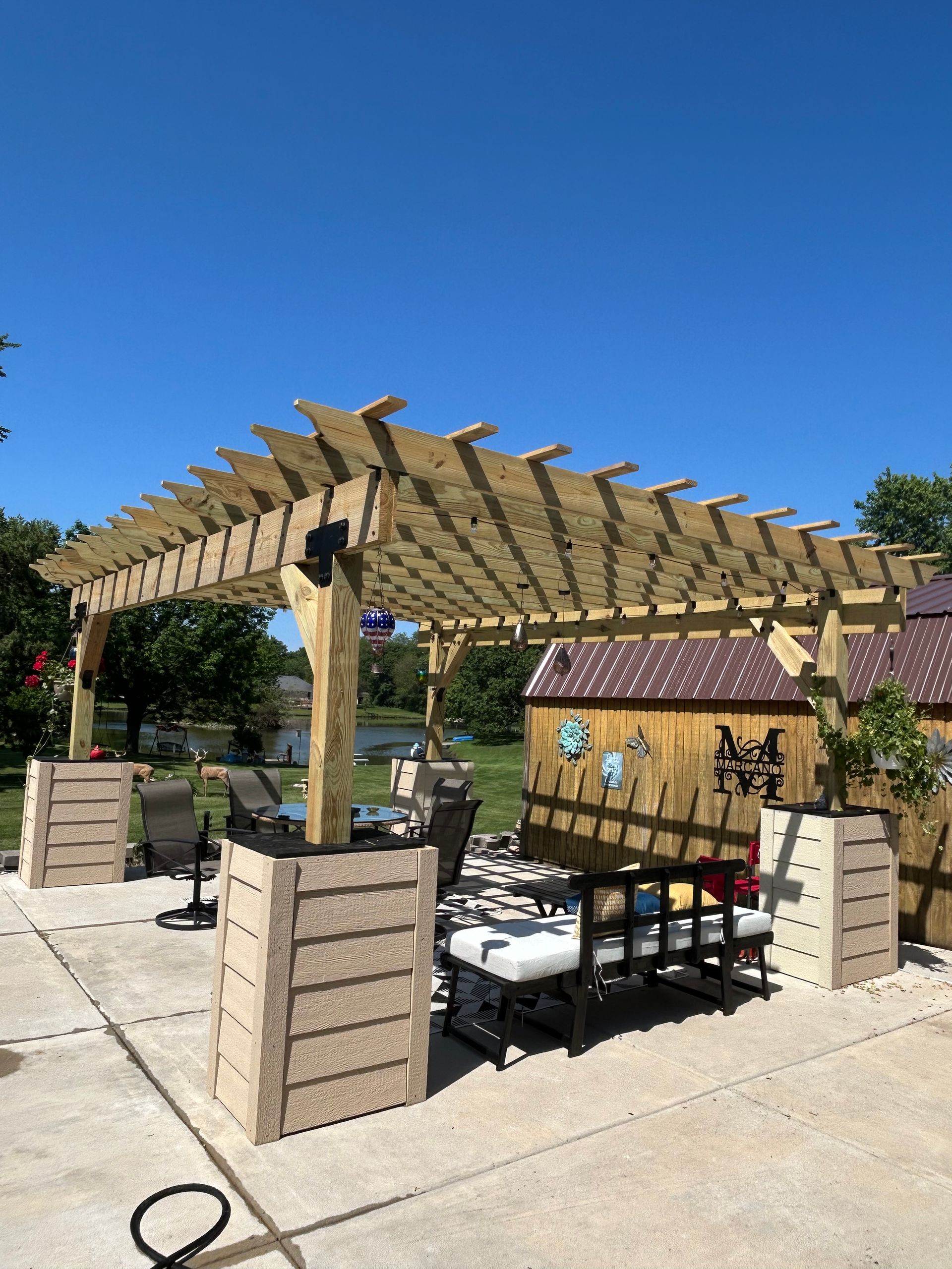 Outdoor wooden pergola and seated patio area on a sunny day under a clear blue sky