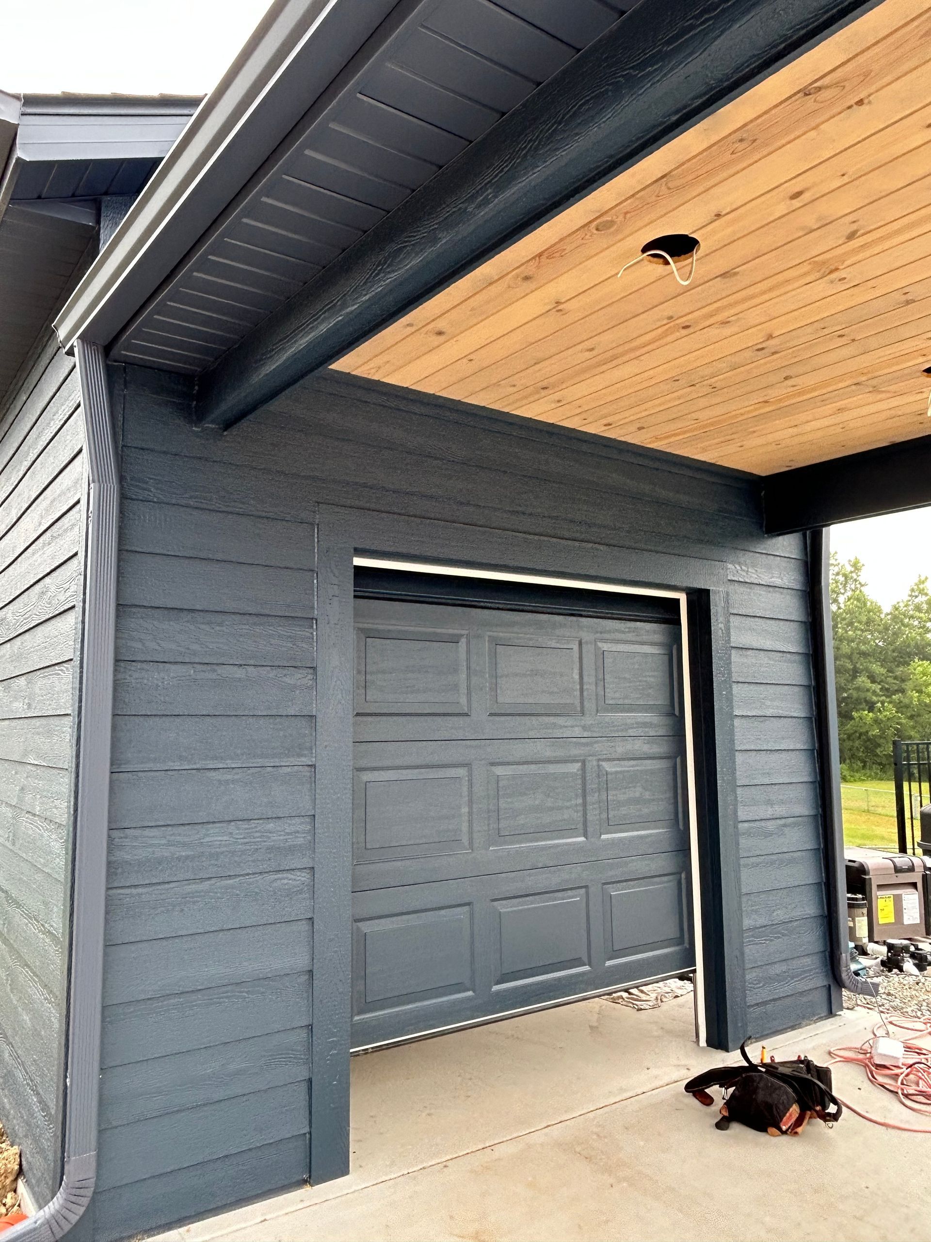 Dark gray house exterior with a partially open garage and a small black dog on the concrete floor