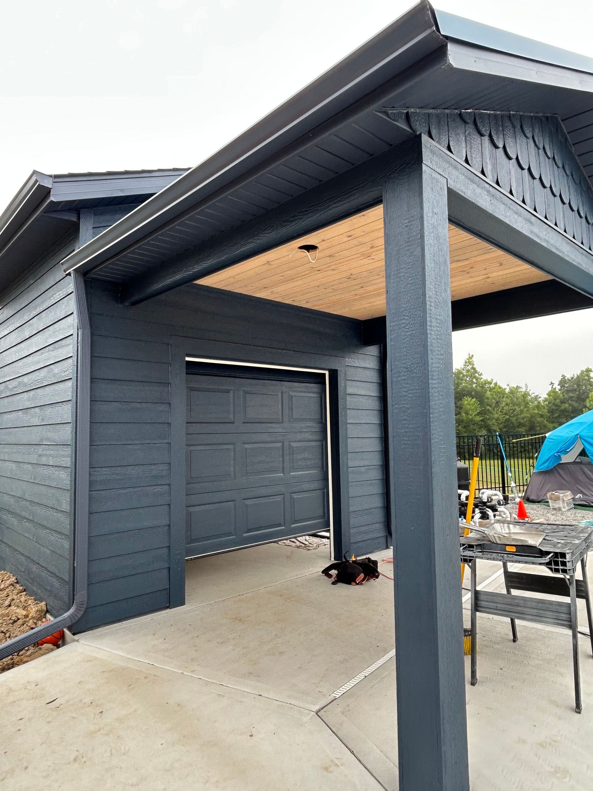 Dark gray house entry with covered porch, garage door, and concrete driveway in front.