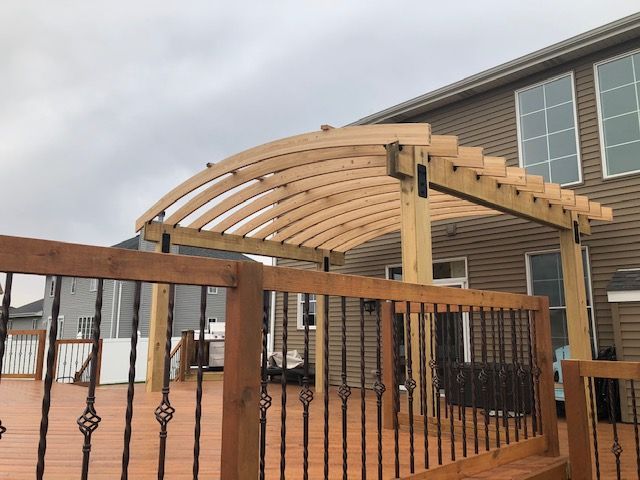 Wooden pergola over a fenced backyard deck beside a house