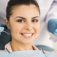 A woman is smiling while getting her teeth examined by a dentist.