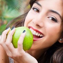 A woman is eating a green apple with her mouth open.