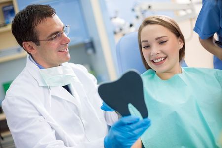 A dentist is looking at a patient 's teeth in a mirror.