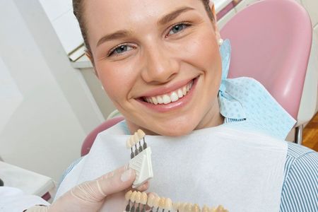 A woman is smiling in a dental chair while a dentist holds a model of her teeth.