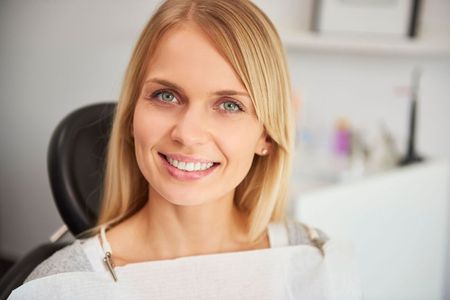 A woman is smiling while sitting in a dental chair.