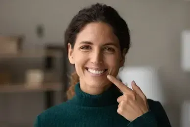 A woman is sitting in a dental chair looking at her teeth in a mirror.