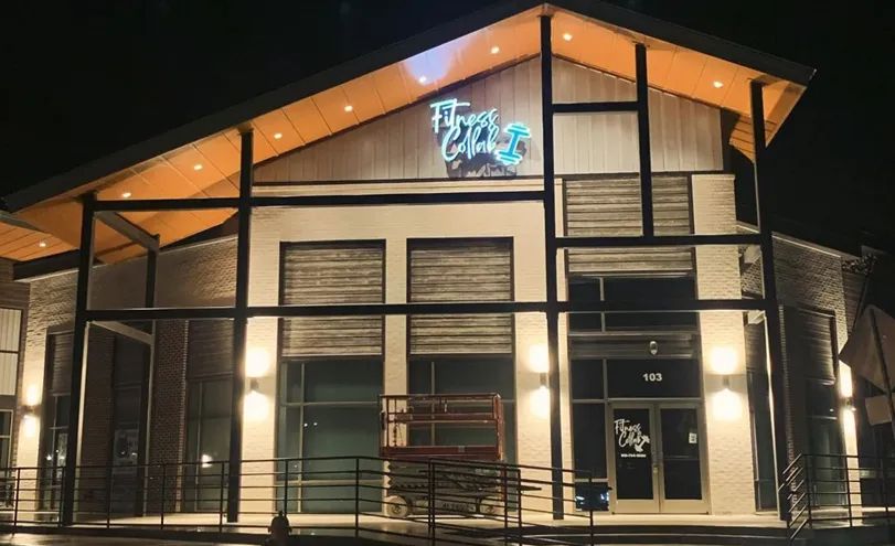 A modern commercial building with a peaked roof and illuminated signage at night.