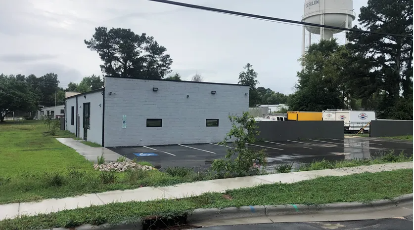 A light-gray commercial building with a black-trimmed parking lot featuring an accessible parking space.