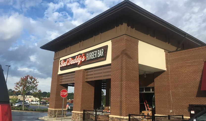 The exterior of a Bad Daddy’s Burger Bar restaurant on a cloudy day, featuring brick architecture and a stop sign.