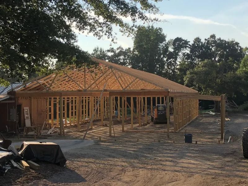 A wood-framed building under construction in a wooded setting with roof trusses installed.