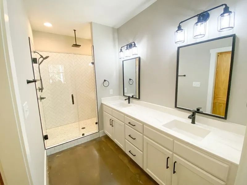 Modern bathroom with a double vanity, white cabinets, black fixtures, and a glass-enclosed walk-in shower.