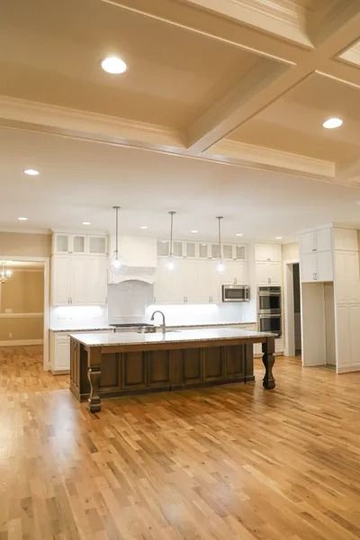 Spacious kitchen with white cabinetry, a large wood-toned center island, hardwood floors, and a coffered ceiling.