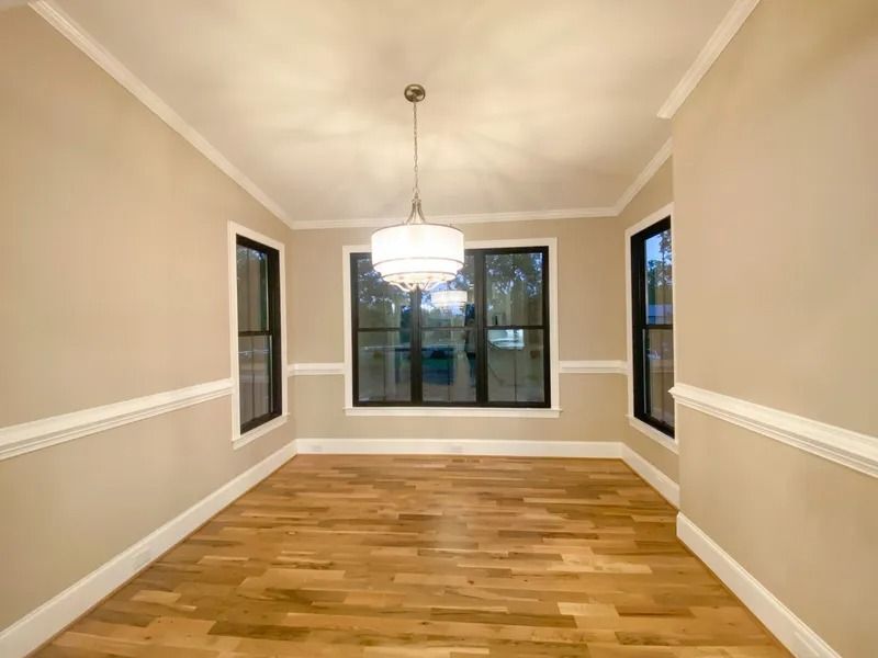 An empty dining room with light beige walls, white trim, a modern chandelier, and polished hardwood floors.