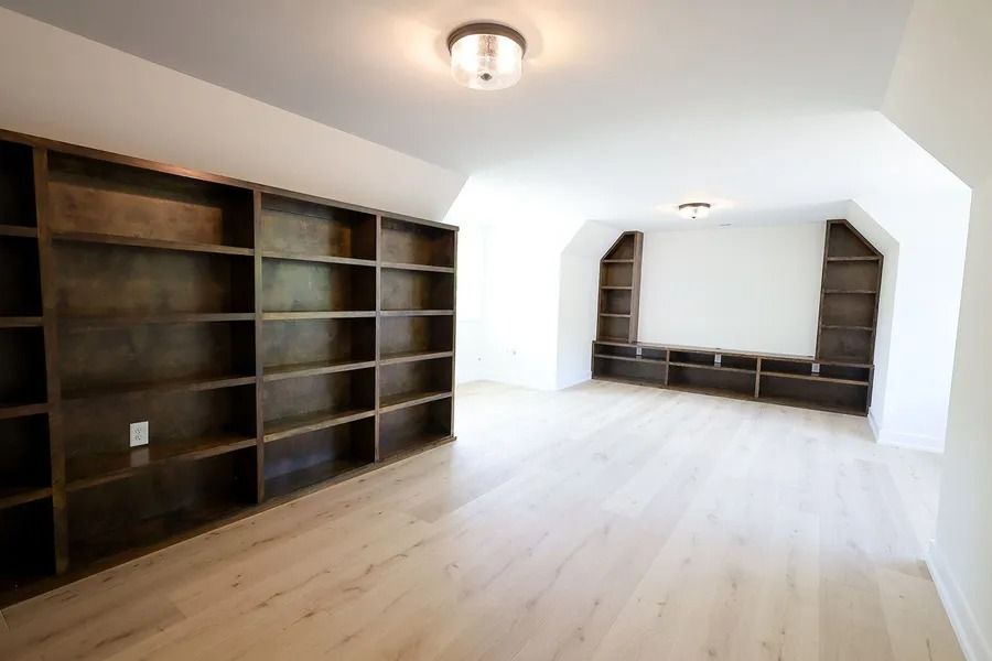 An empty room with light wood floors, high white sloped ceilings, and built-in dark wood bookshelves on two walls.