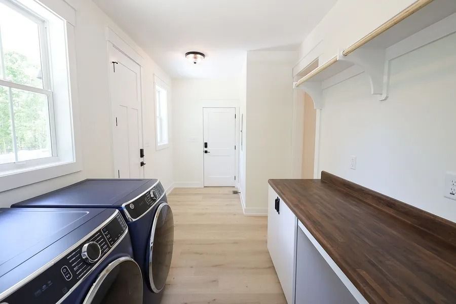 Laundry room with blue appliances, a wooden countertop, and light wood flooring leading to a white door.