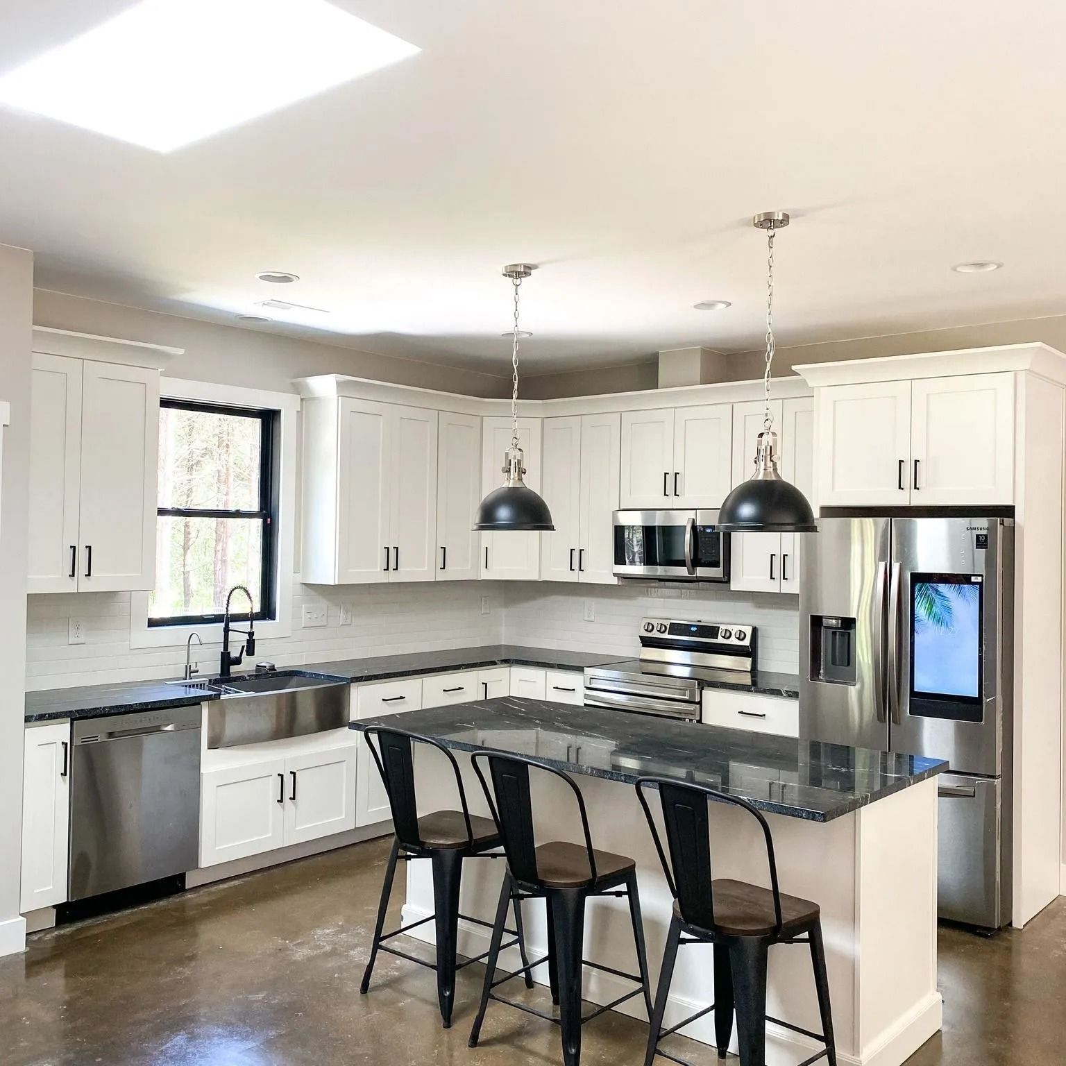 Modern kitchen with white cabinetry, stainless steel appliances, a dark granite island, and two pendant lights.