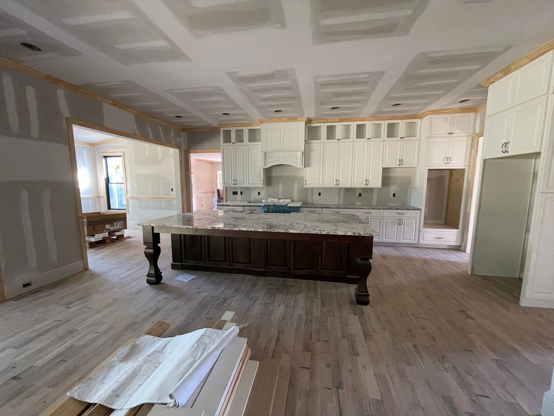 A kitchen under construction with white cabinets, a large dark wood island with a marble top, and unfinished drywall.