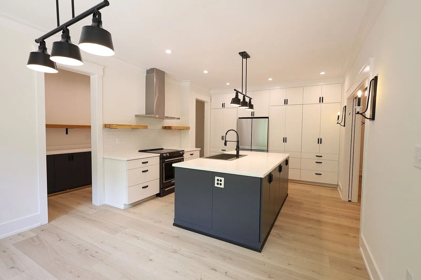 A modern kitchen with a dark grey central island, white cabinetry, light wood floors, and industrial-style pendant lights.