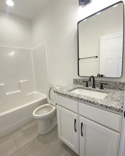 A clean bathroom with a white vanity, speckled granite countertop, black-framed mirror, toilet, and a white tub shower.