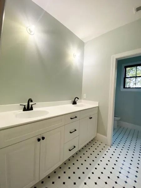 A bright, modern bathroom featuring a white double-sink vanity, matte black faucets, pale blue walls, and tiled flooring.