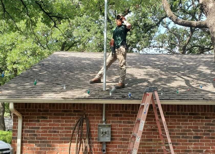 A man is standing on top of a roof next to a ladder.