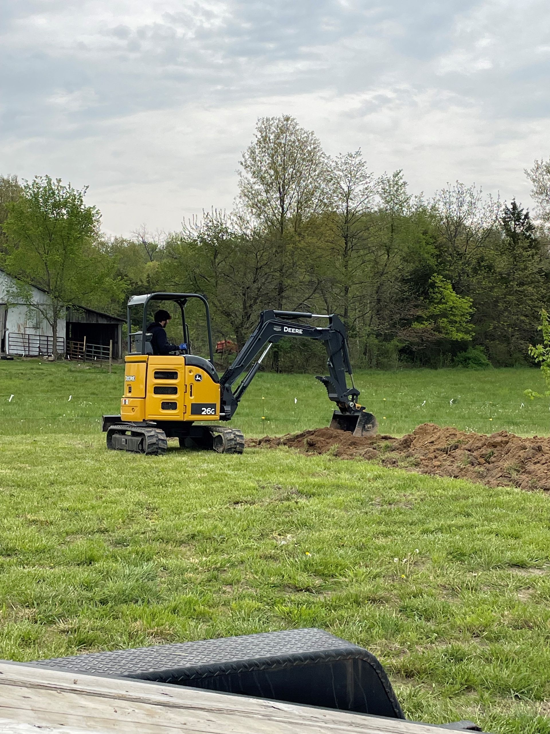 a yellow excavator is digging a hole in a grassy field .
