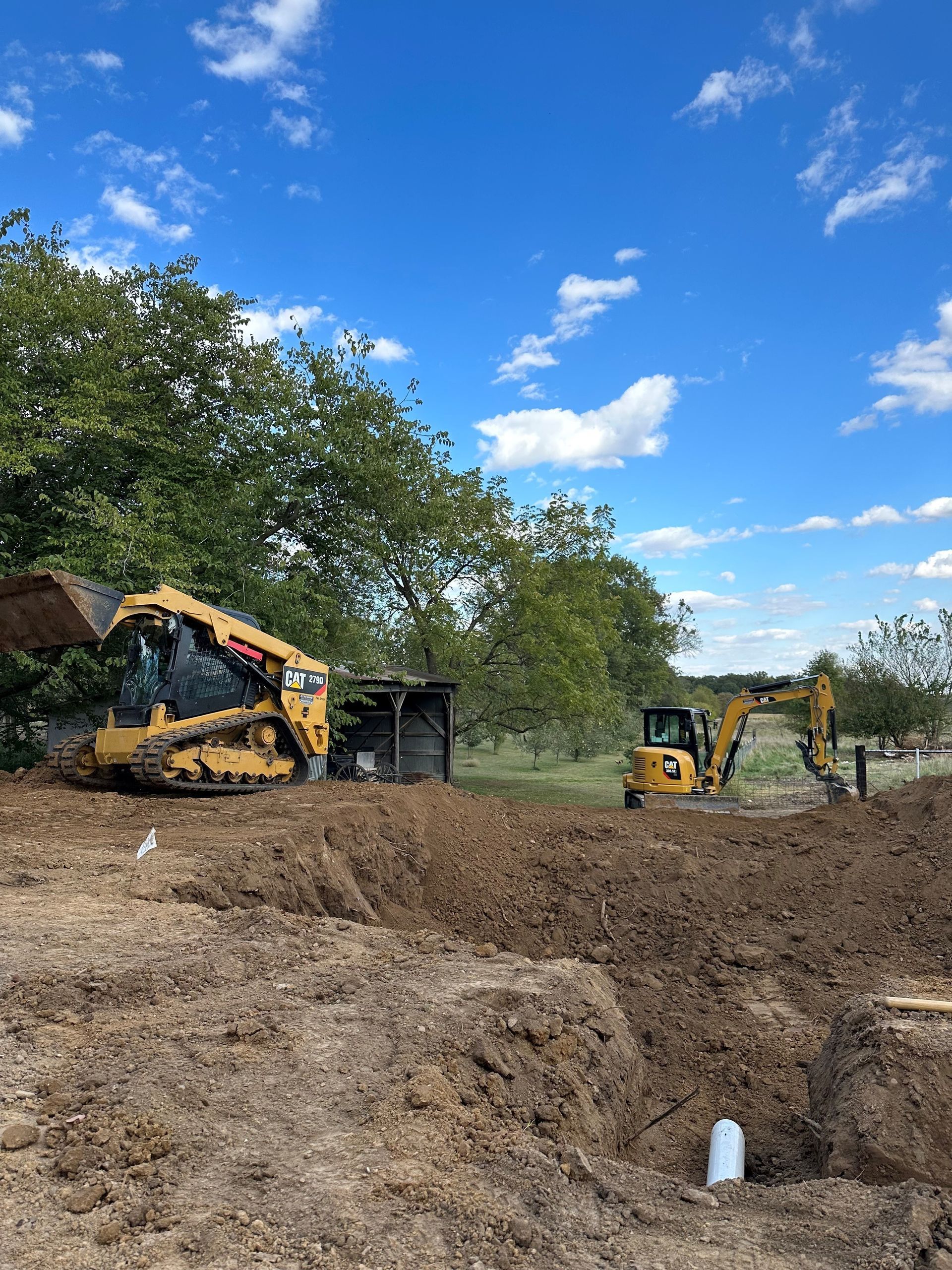 a bulldozer and an excavator are working on a dirt field .