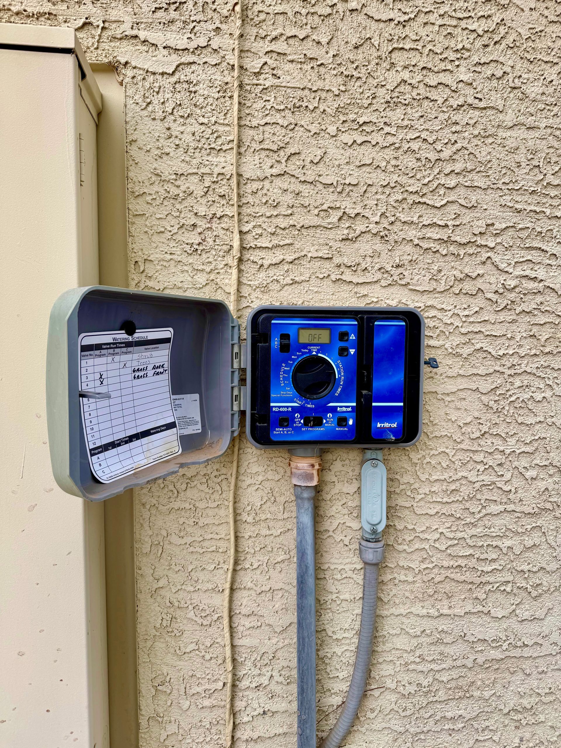 A sprinkler controller is mounted on the side of a building.
