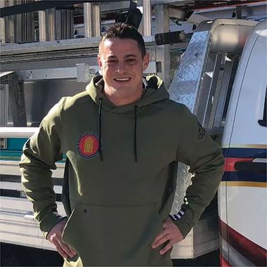 Man in green hoodie standing beside a white van, smiling with hands on hips.