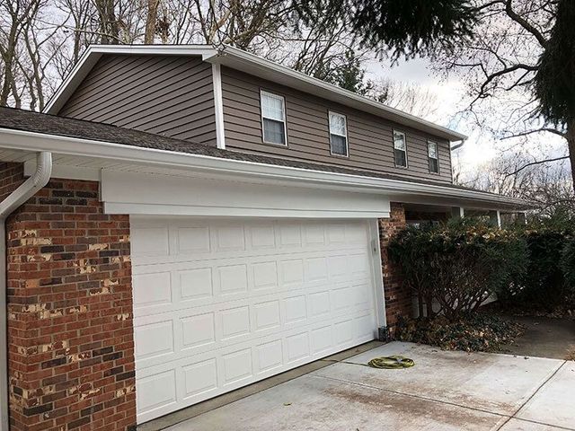 Two-story house exterior with a white garage door, brick siding, and a concrete driveway.