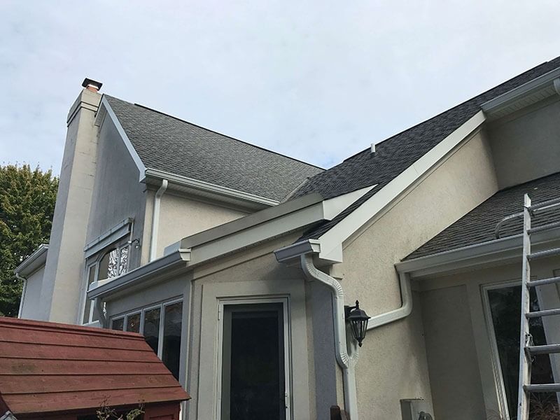 Suburban house exterior with gray siding, gabled roof, and front entry under overcast sky
