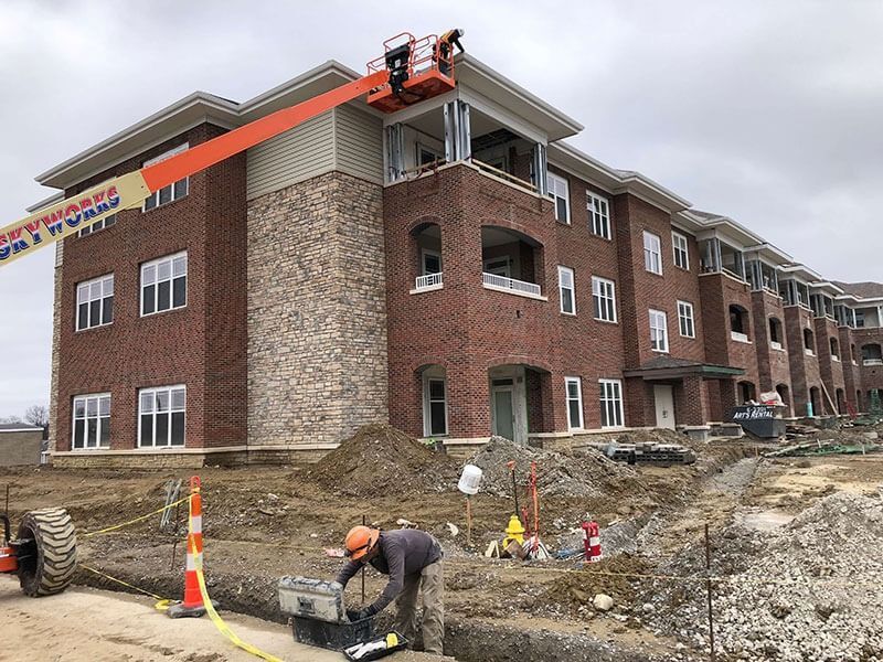 Construction site with brick apartment building, workers, and orange lift on the roof