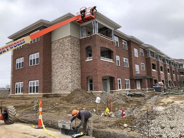 Apartment building under construction, with workers, scaffolding, and an orange lift on the roof.
